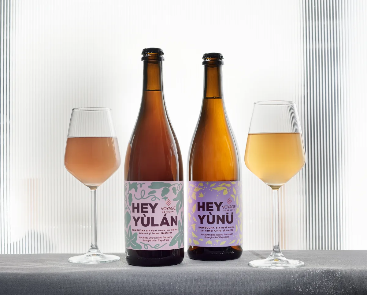Two bottles of Voyage Kombucha — Hey Yùlán and Hey Yùnü — beside filled glasses on a lavender backdrop