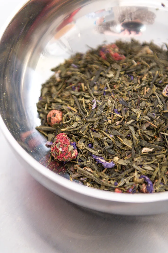 A bowl of green tea infused with botanicals, berries, and flower petals