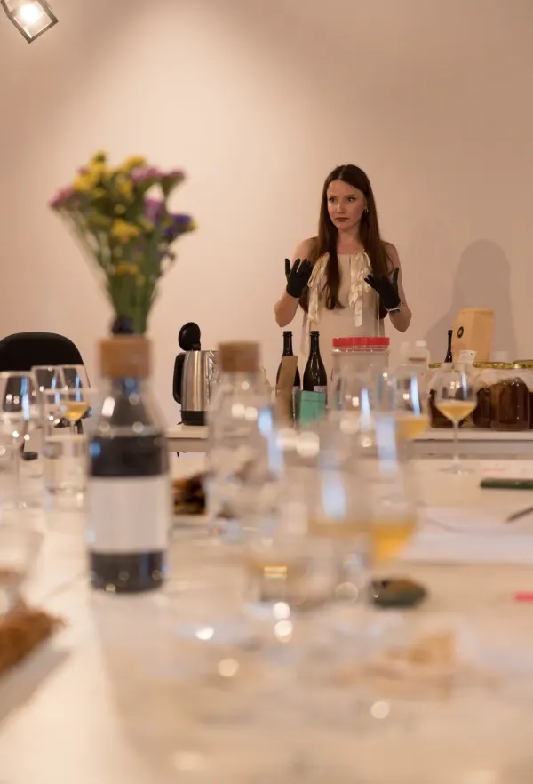Ioana, wearing black gloves, explaining the fermentation process behind a table of bottles, jars and a kettle