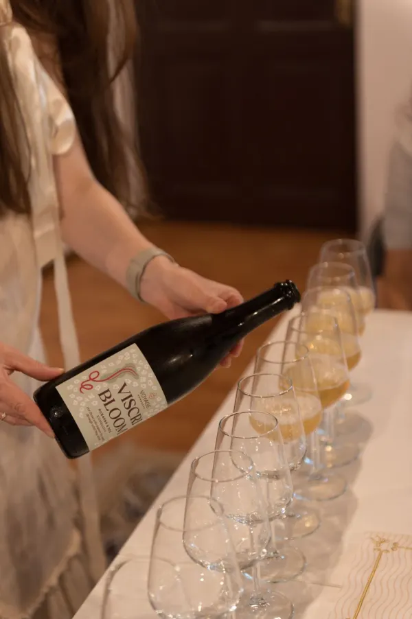 Ioana presenting a bottle of Viscri Bloom kombucha beside a row of tasting glasses